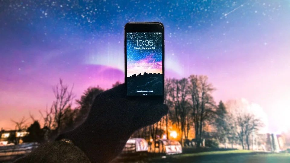 Gece gökyüzüne doğru tutulan bir akıllı telefon, arkada yıldızlar ve ağaçlar