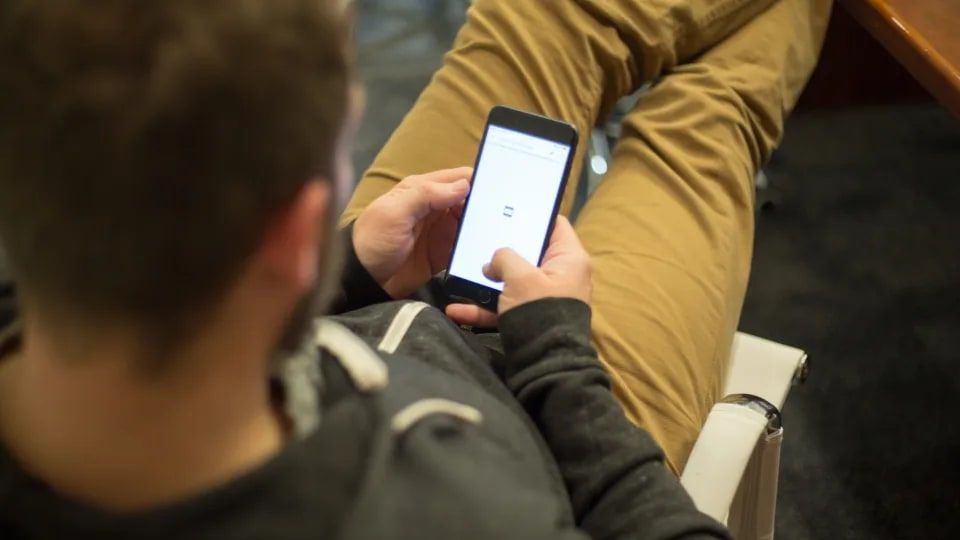Koltukta oturan bir adamın omzunun üzerinden görünen, iki eliyle tuttuğu telefon