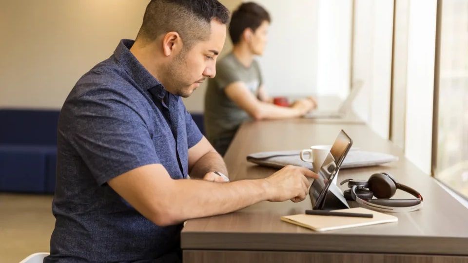 Ofiste tablet ve kulaklıkla masada çalışan bir erkek