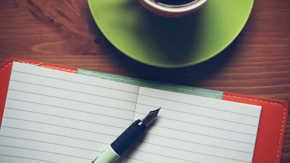 Açık bir çizgili defter, dolma kalem ve yeşil tabaklı bir fincan