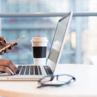 Kahve bardağının yanında telefon ve dizüstü bilgisayar kullanan eller