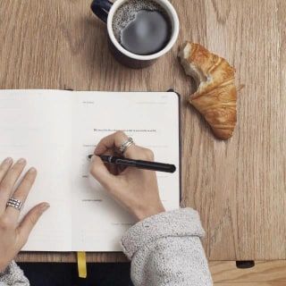 Kahve ve kruvasanın yanında deftere not alan eller