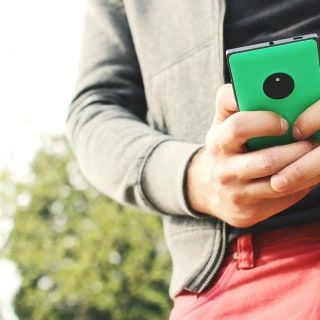 Yeşil bir akıllı telefonu iki eliyle tutup ekrana yazan bir kişi