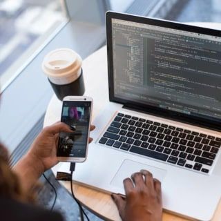 Yuvarlak masada telefon ve dizüstü bilgisayar kullanan eller, yanında kahve